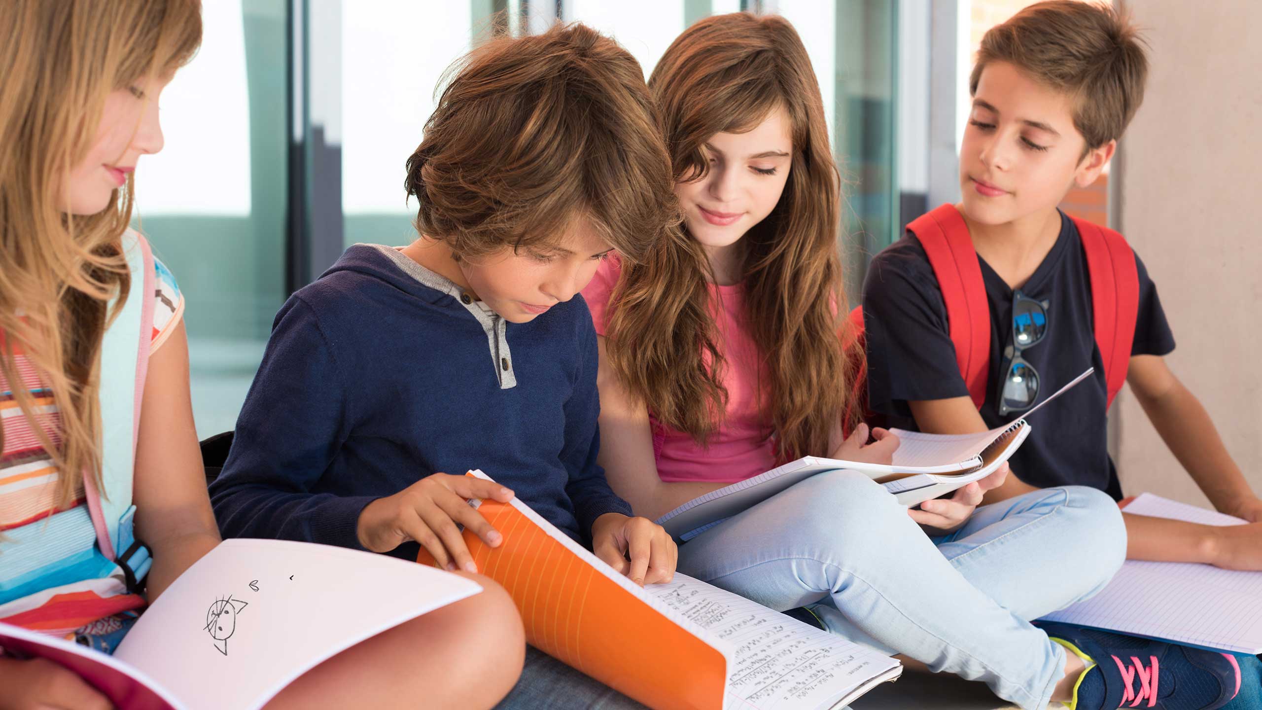 Four little kids sit together reading texts. Elementary education.