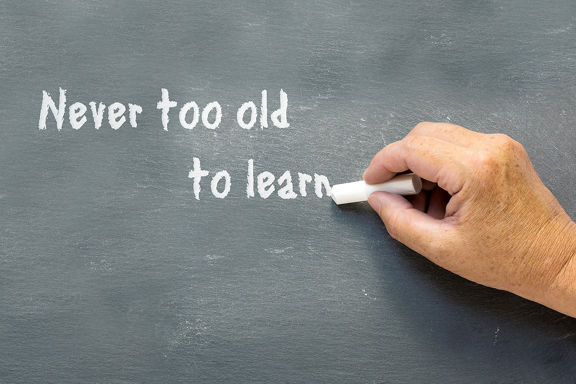 Image of chalkboard with words " Never too old to learn" with a hand holding chalk.