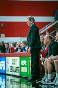 Photo of Casper College Women's Basketball team, Dwight Gunnare, standing, and Assistant Head Coach Nate Macy watch the game from the sidelines.