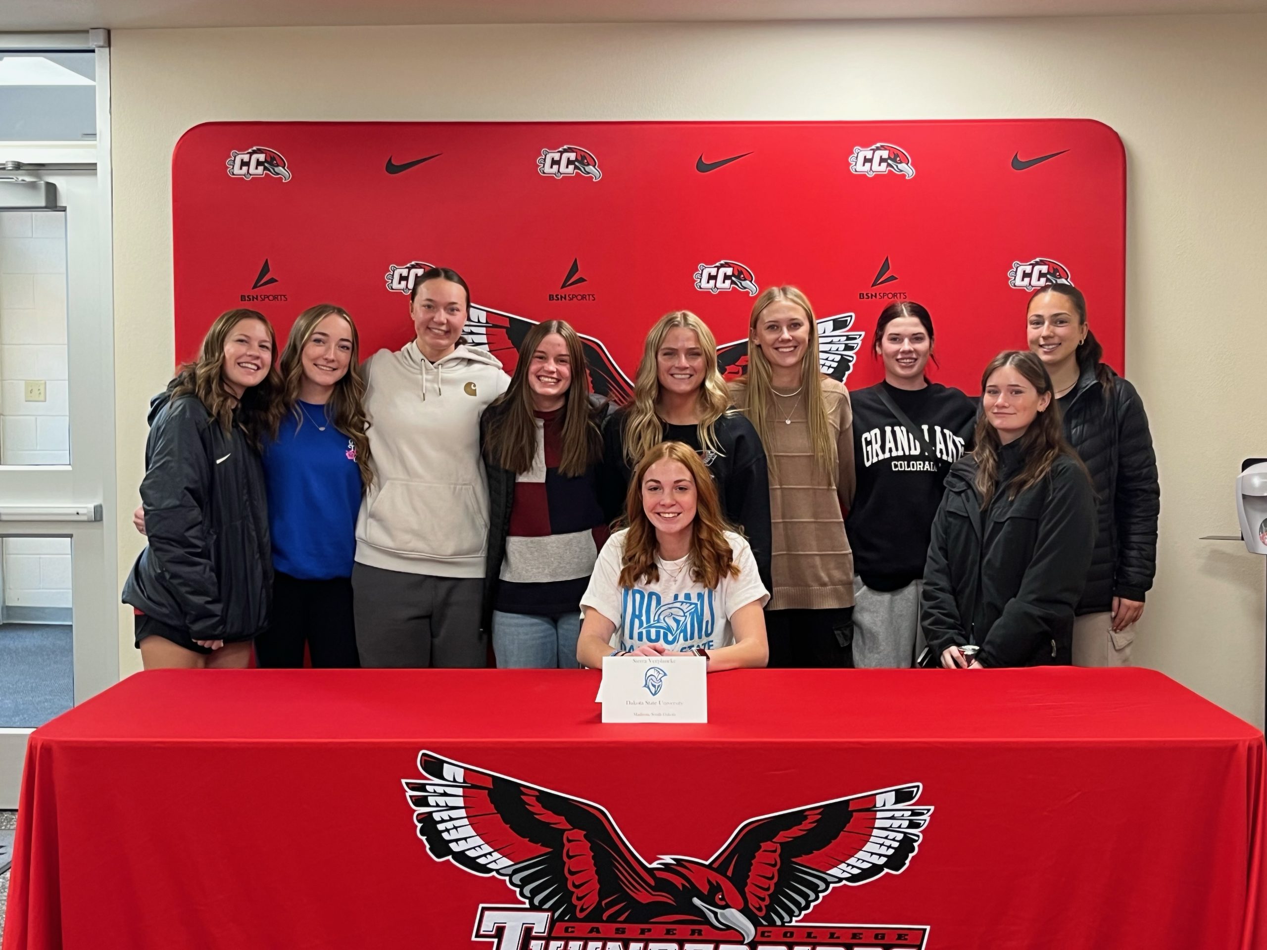 Photo of members of the Casper College Women's Soccer team behind Sierra Verplancke signing a letter of commitment to Dakota State University.