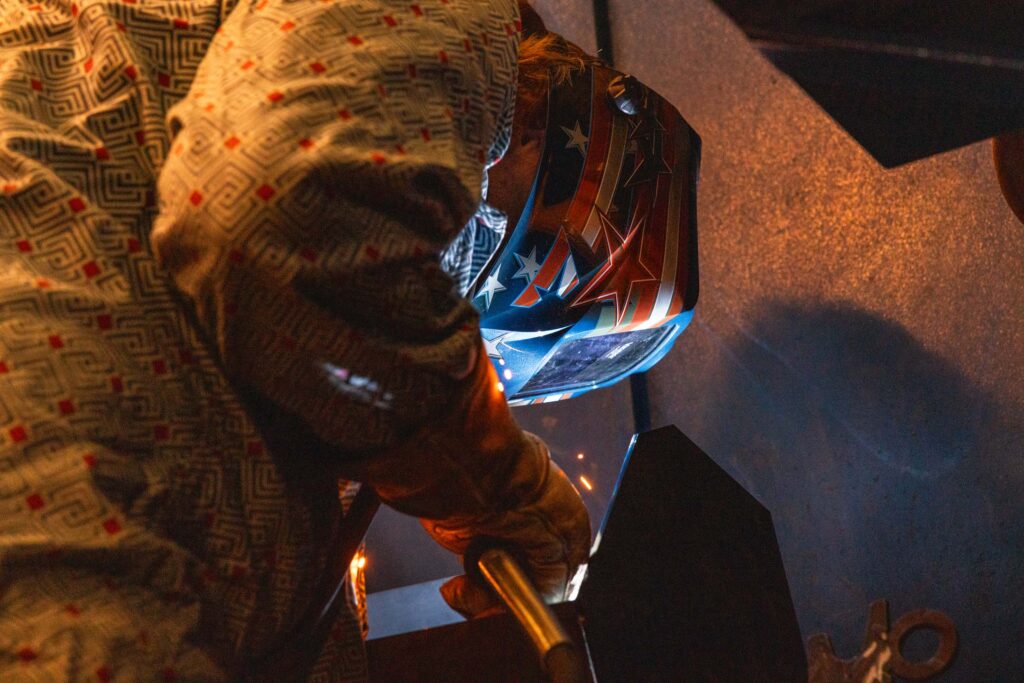A person in welding gear welding two pieces of metal together