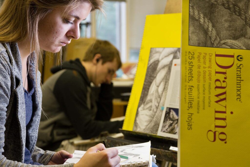 Fine arts students concentrate on drawing assignments in a studio classroom.