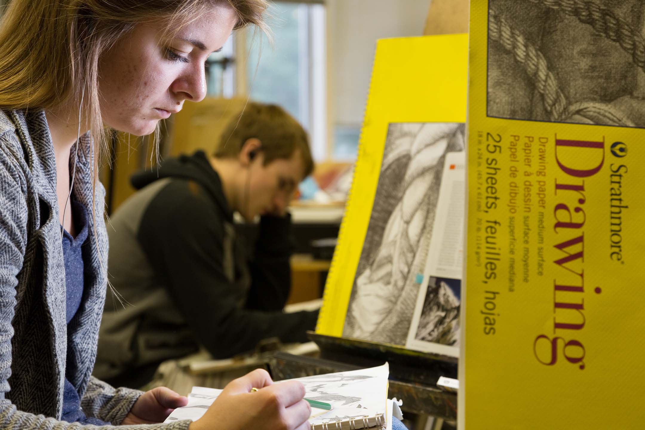 Fine arts students concentrate on drawing assignments in a studio classroom.