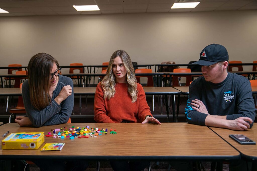 Two women and a man sitting at a table with legos learning about economics