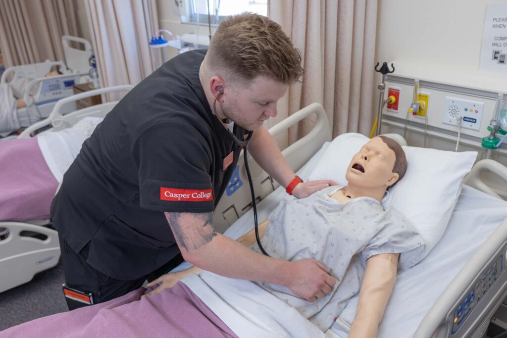 A student checks the heartbeat of a test dummy in the health science sim center