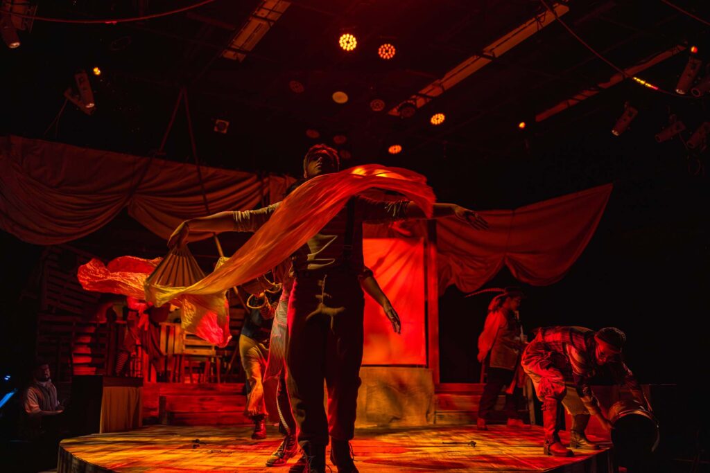 Actors perform a dramatic ensemble scene with flowing fabric and theatrical lighting during a Casper College theatre production.
