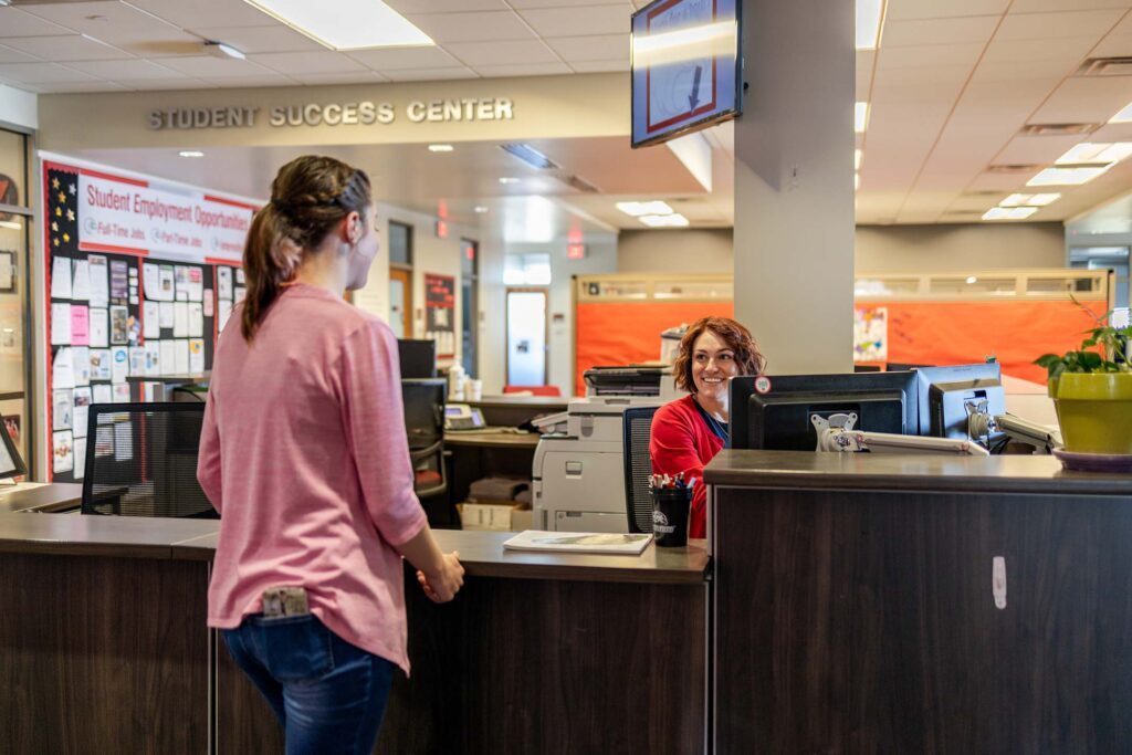 Student speaks with a staff member at a front desk inside a campus Student Success Center.