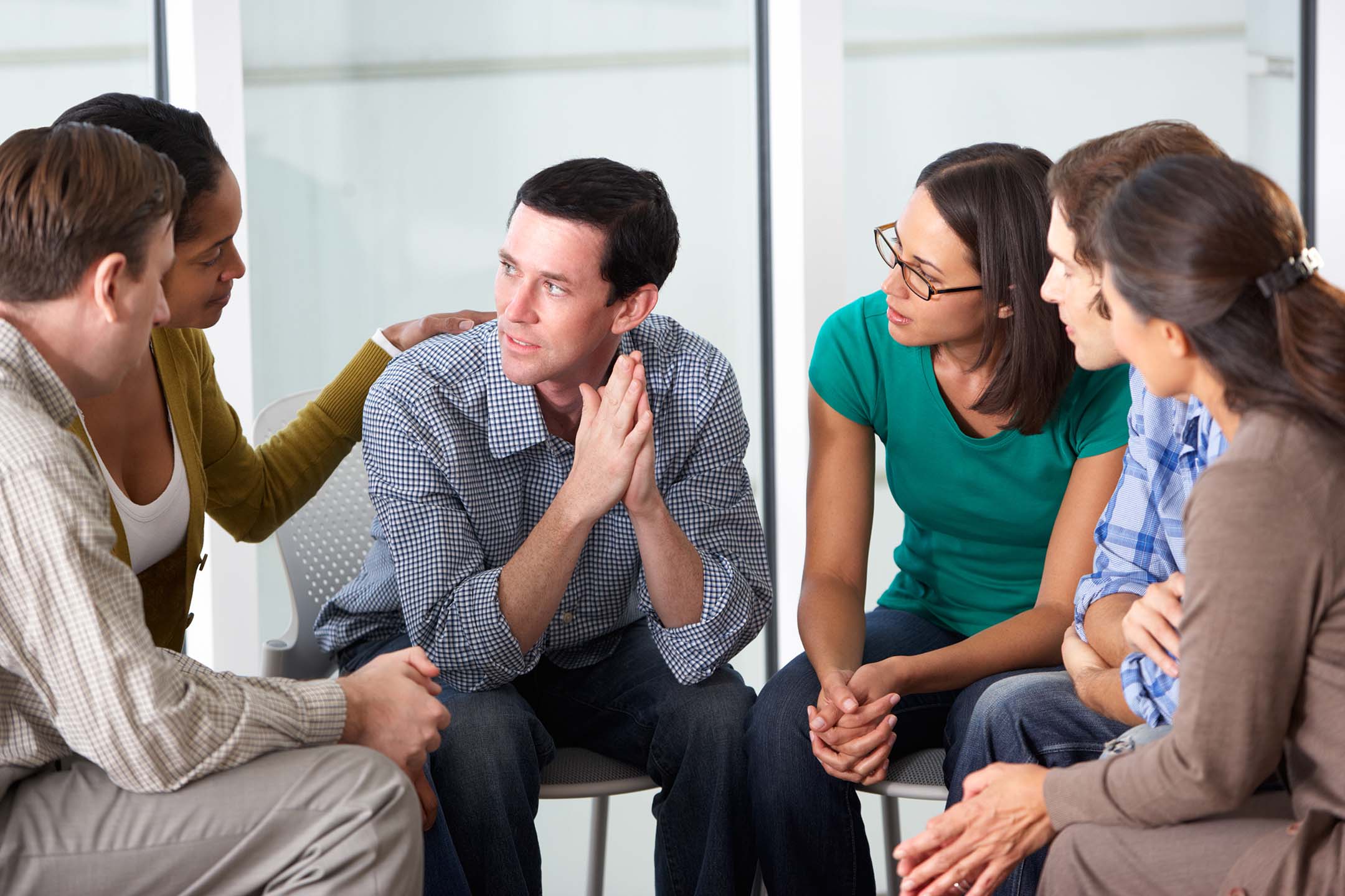 Small group counseling session with four adults seated in a circle, talking in a bright room. This describes addiction studies