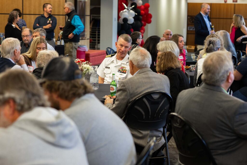 People at round tables chatting and sharing drinks in a decorated indoor event space.