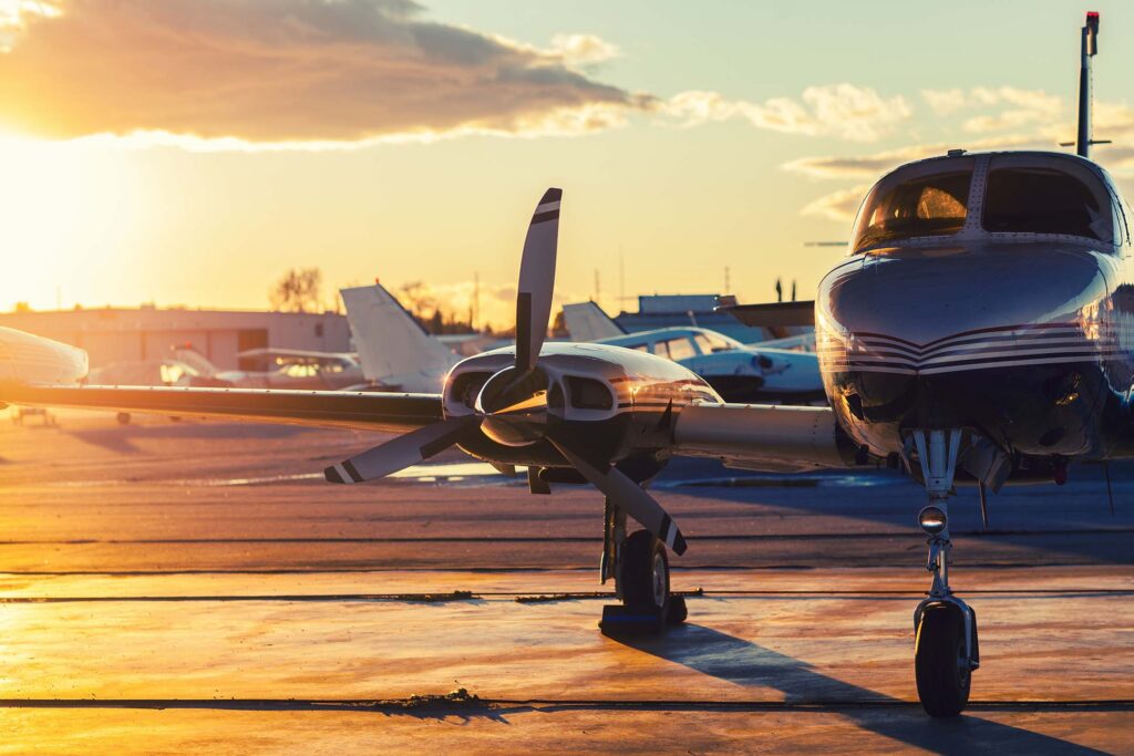 Small airplane parked on a runway at sunrise with other aircraft nearby ready for an aviation course.