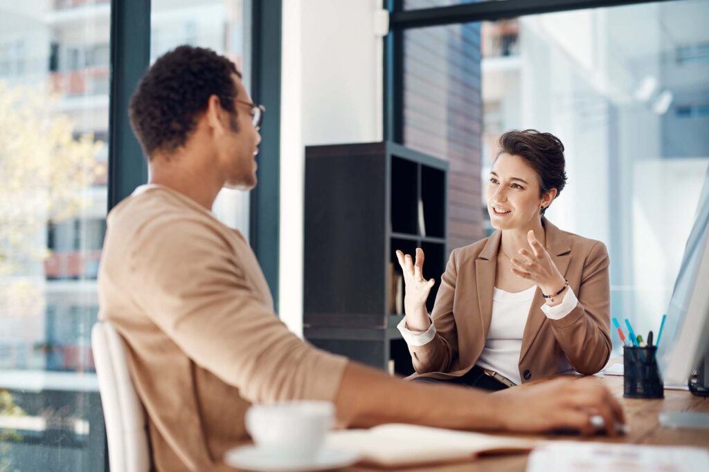 Two coworkers in conversation across a conference table in a bright office. Business Management