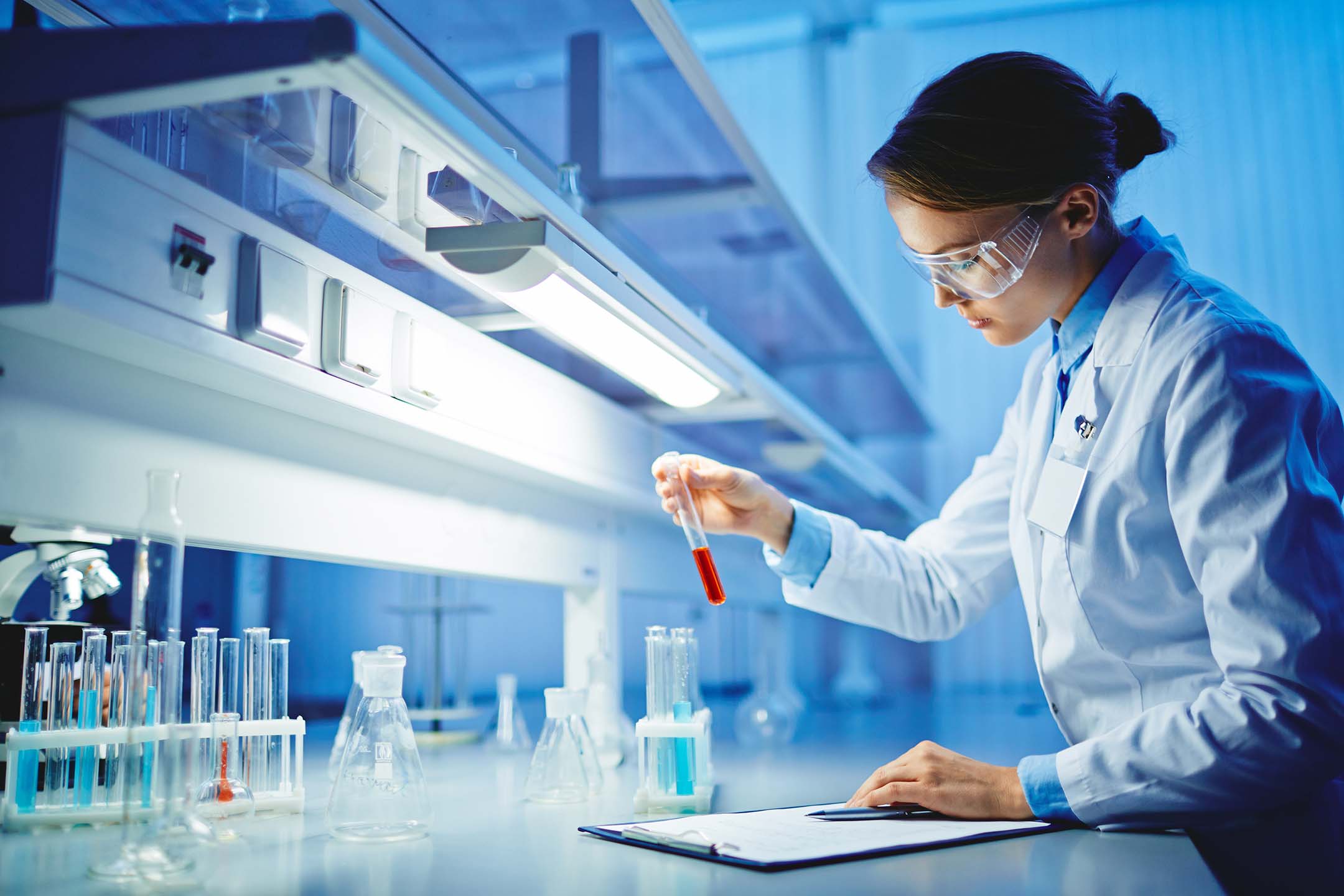 Scientist in a lab coat working with test tubes under bright laboratory lighting doing chemistry.