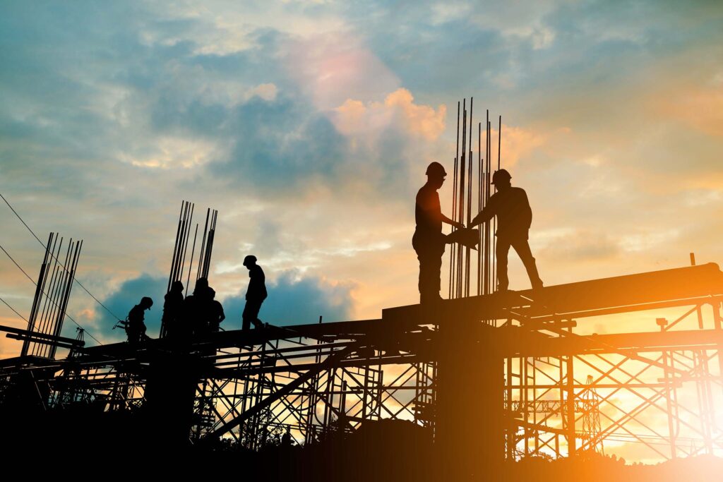 Silhouetted construction workers standing on a steel structure at sunset. Construction management