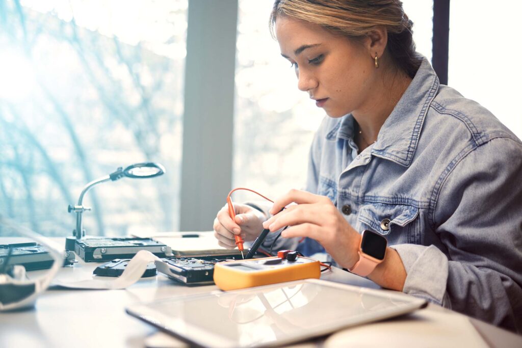 Student soldering or assembling a small electronics device at a workbench.