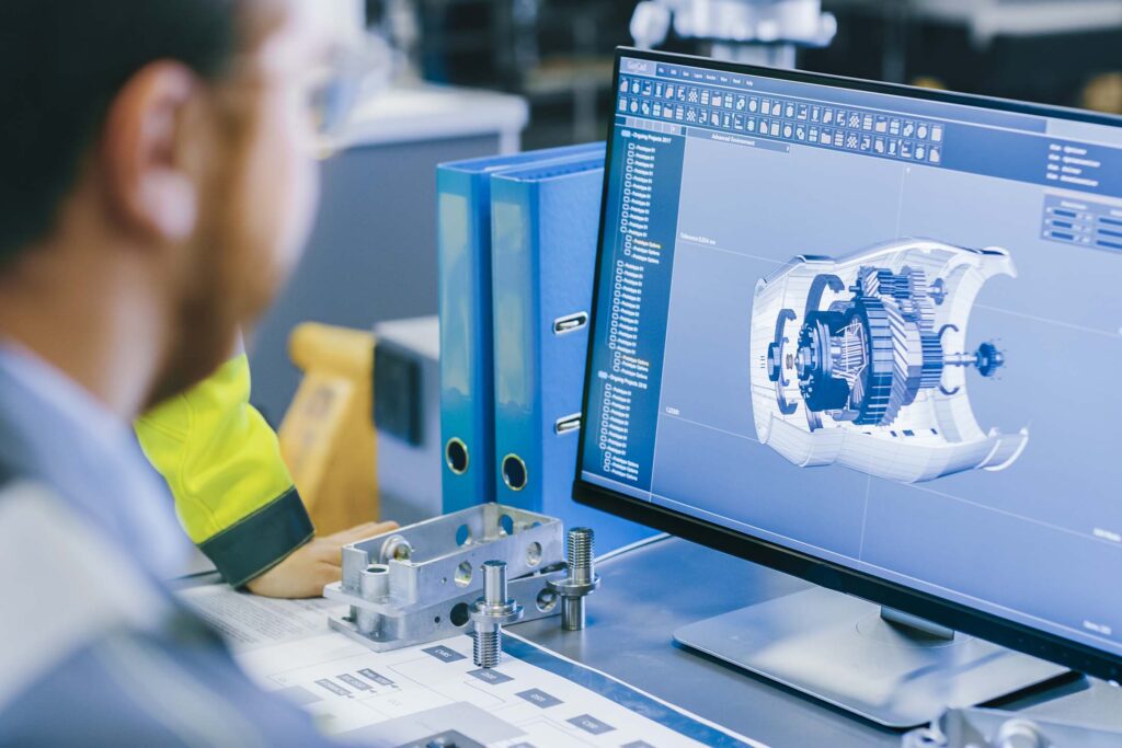 Person viewing a 3D mechanical design on a computer monitor in a workshop. Engineering technology