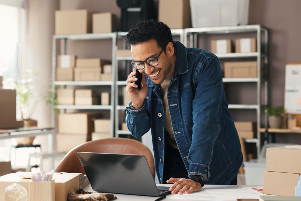 Small business owner speaking on the phone while leaning over a counter in a shop or studio about entrepreneurship.