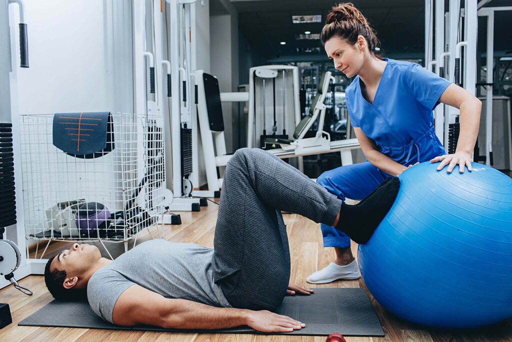 Trainer guiding a person exercising with a large balance ball in a gym. Kinesiology