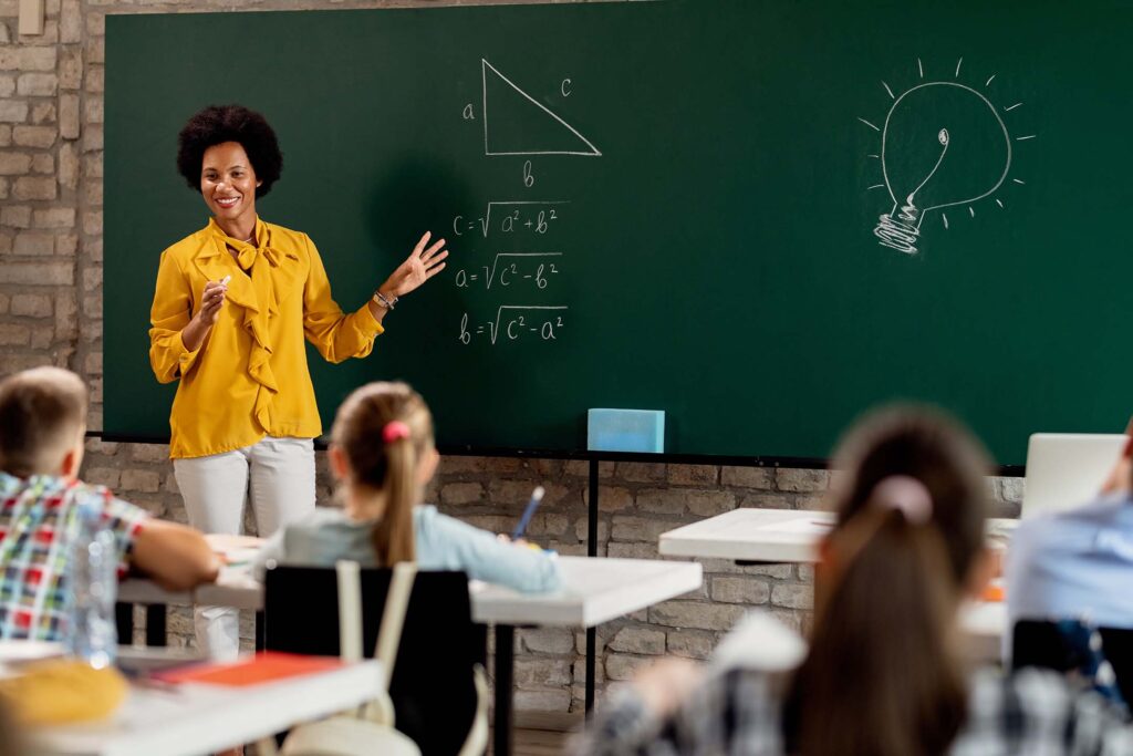 Teacher standing at a chalkboard teaching math to a classroom of students. Secondary Education