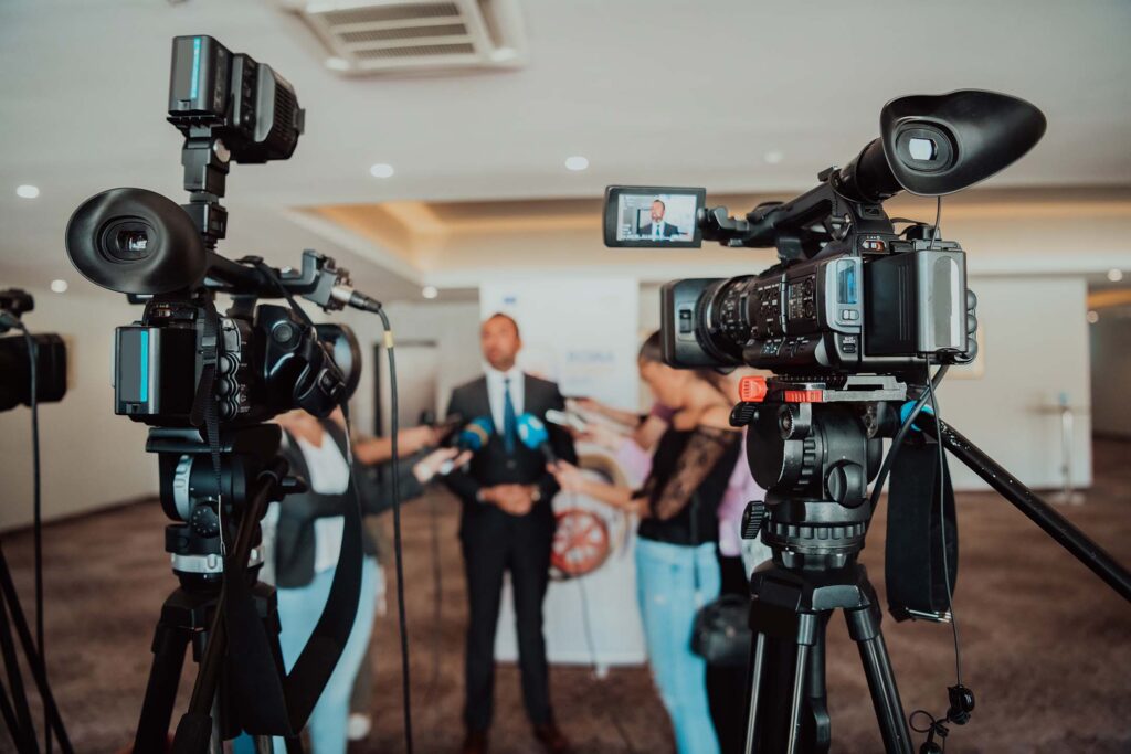 Video cameras filming a speaker at an indoor event for communication classes.