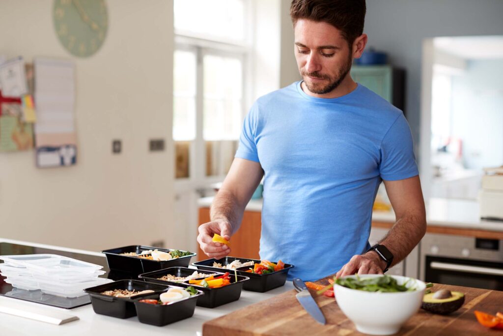 Person preparing meal containers and fresh food in a kitchen. Nutrition