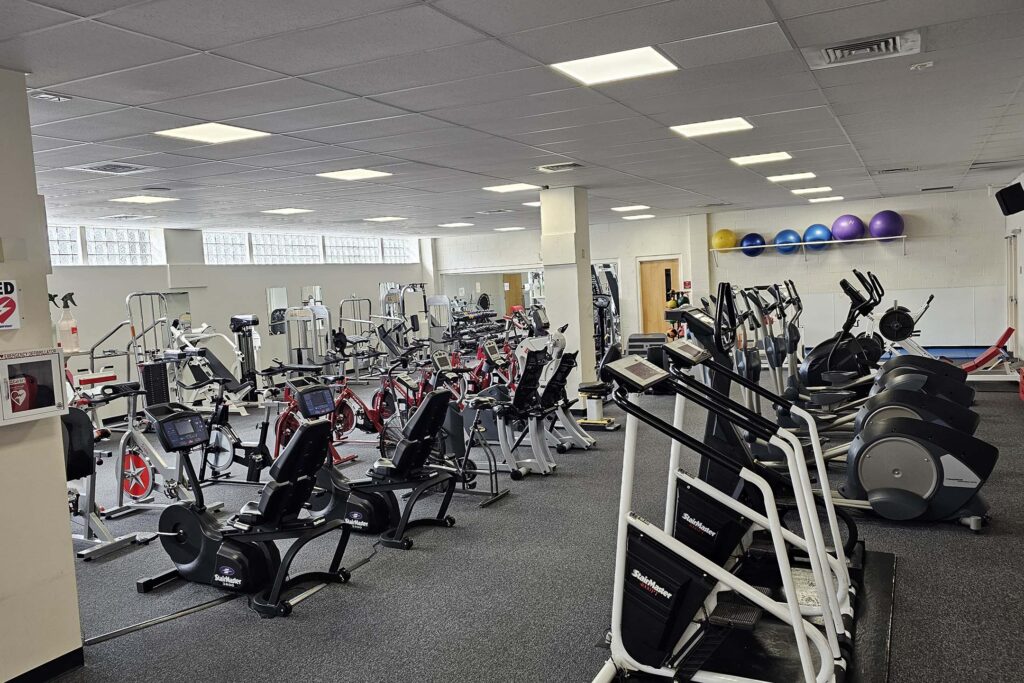 Wide view of an indoor fitness room filled with exercise equipment. Physical education