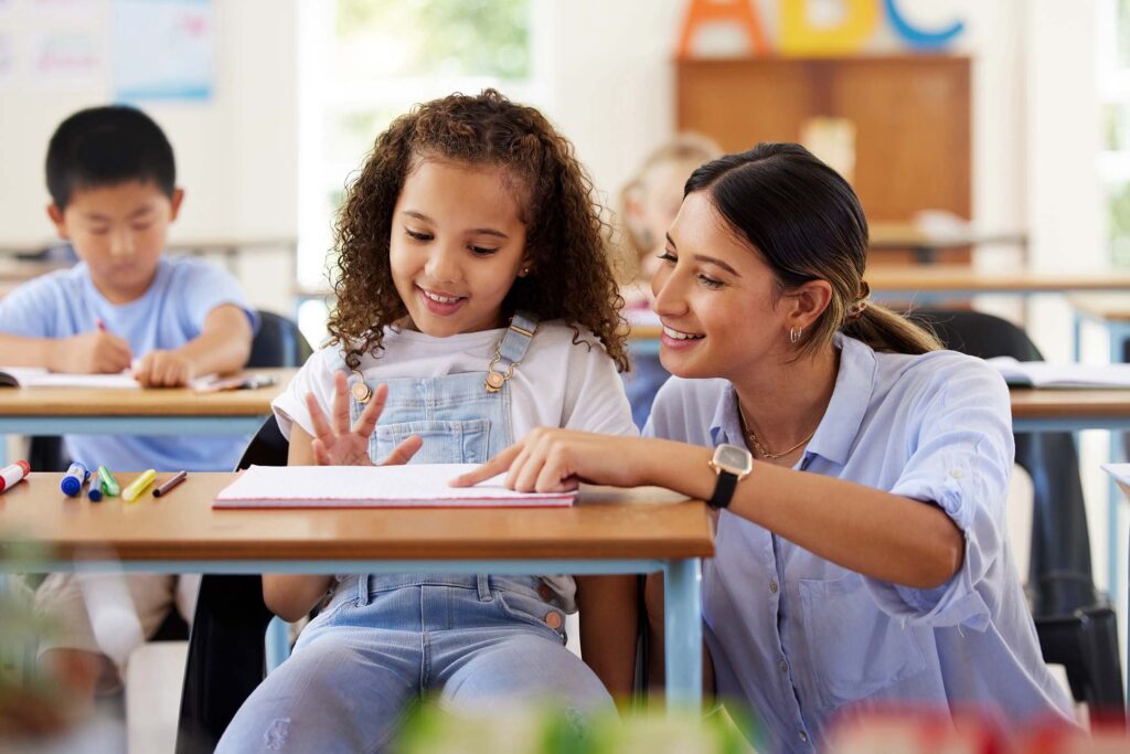 Teacher helping elementary-age students with thier social studies schoolwork at desks.