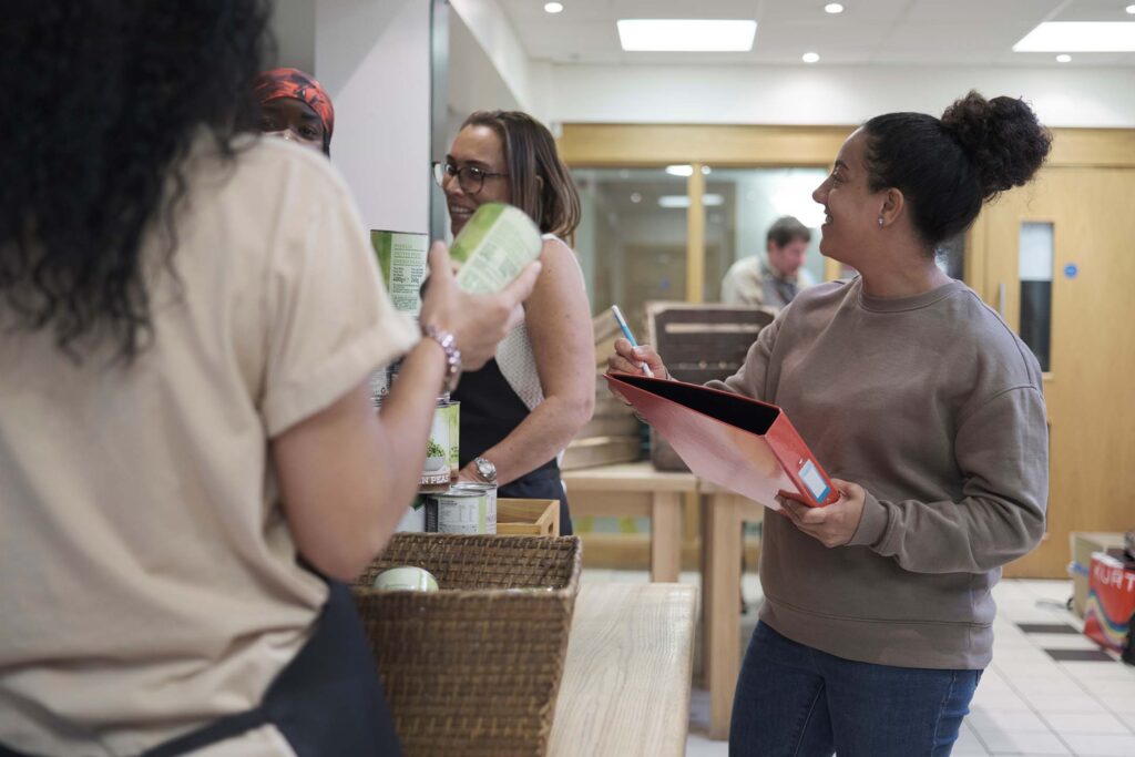 Two people speaking in a hallway or community setting, one holding a clipboard for social work.
