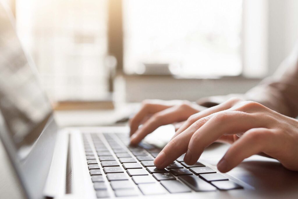 Close-up of hands typing on a laptop keyboard in a softly lit indoor workspace.