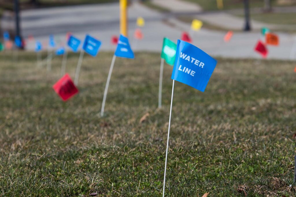 Small colored utility flags marking underground lines in a grassy area. utility locator