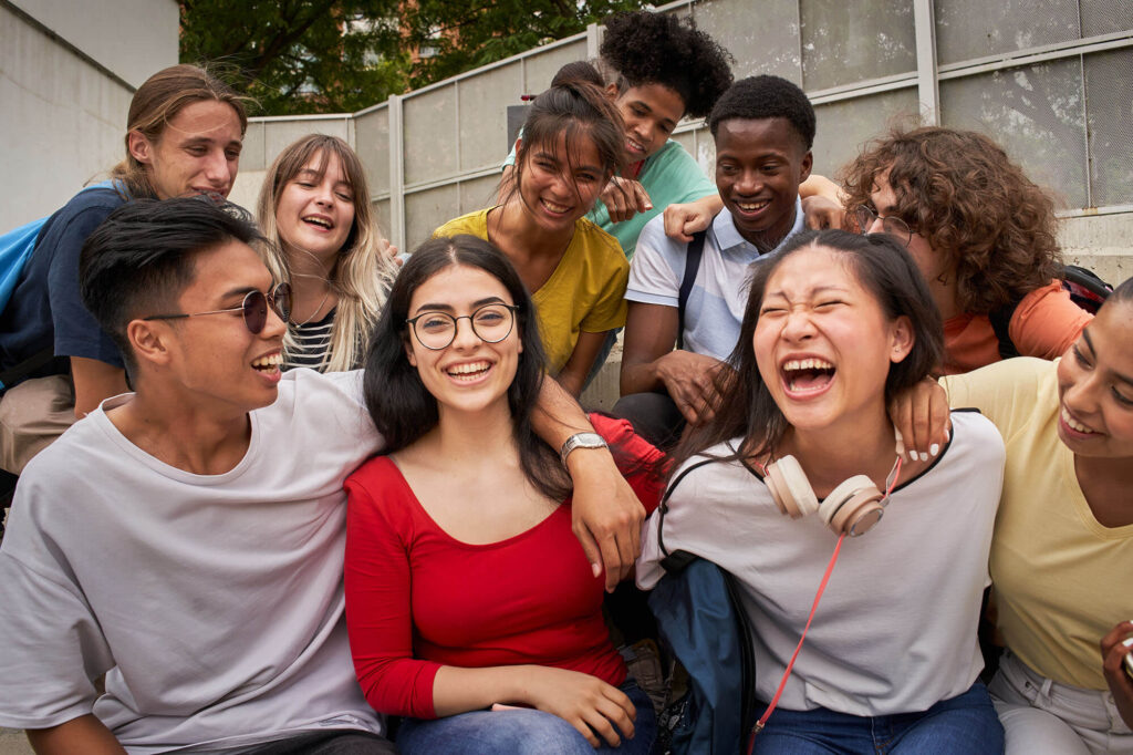 A diverse group of multiethnic high school teenagers laughing and smiling closely together outdoors.