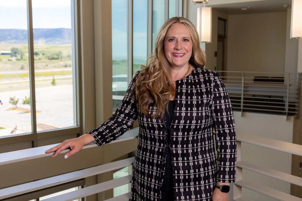 Alicia Roberts, the new human resources director at Casper College, smiling and wearing a black and white patterned jacket while leaning against a fourth-floor railing overlooking the campus.