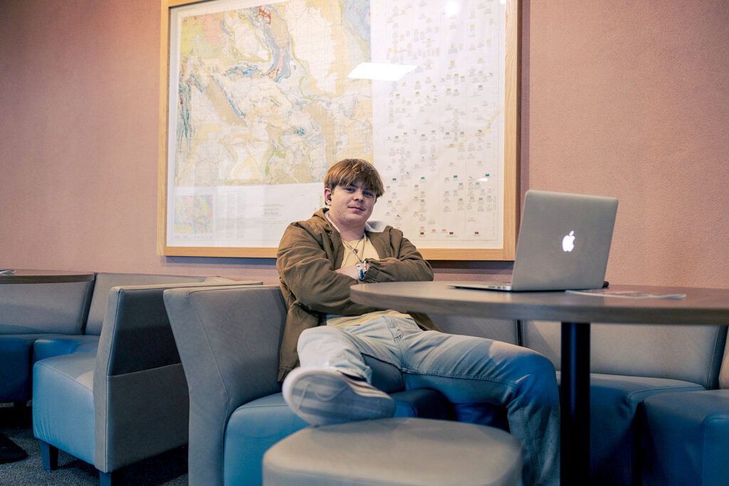 Casper College student studying with a laptop under a large geological wall map in the Wold Physical Science Center.