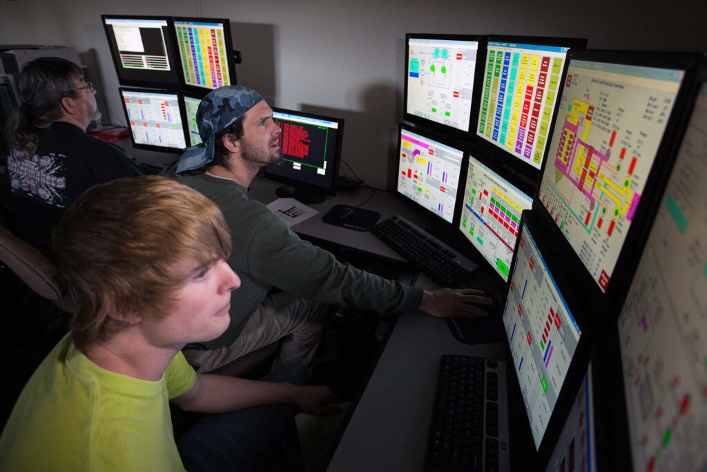Students monitor industrial control systems using multiple computer displays in a process technology lab.