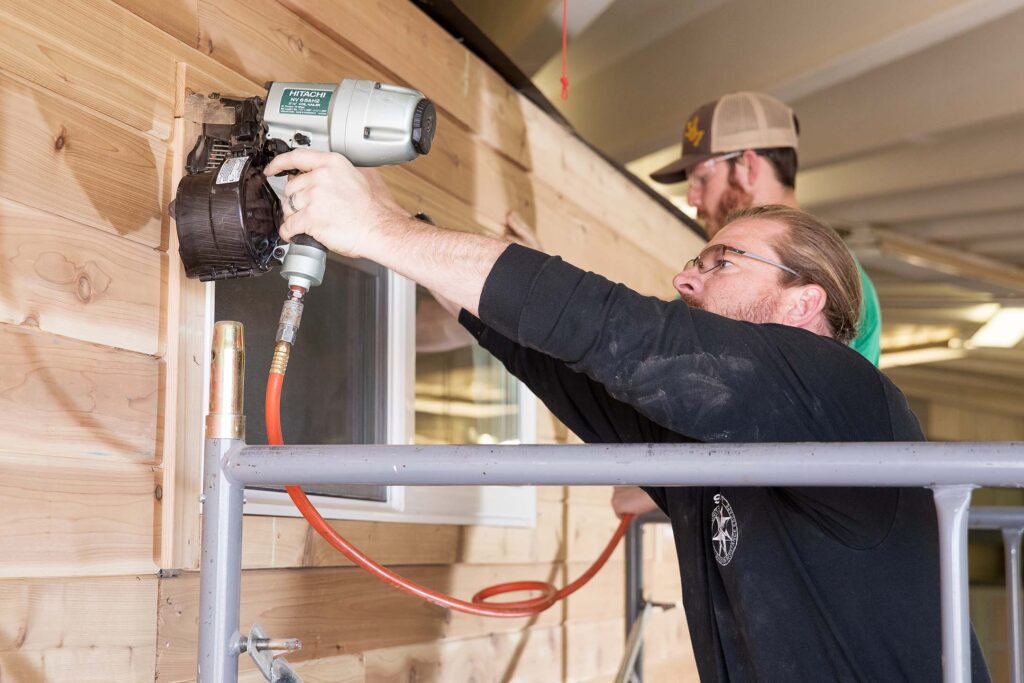 Students install exterior siding with a pneumatic nail gun during hands-on construction training.