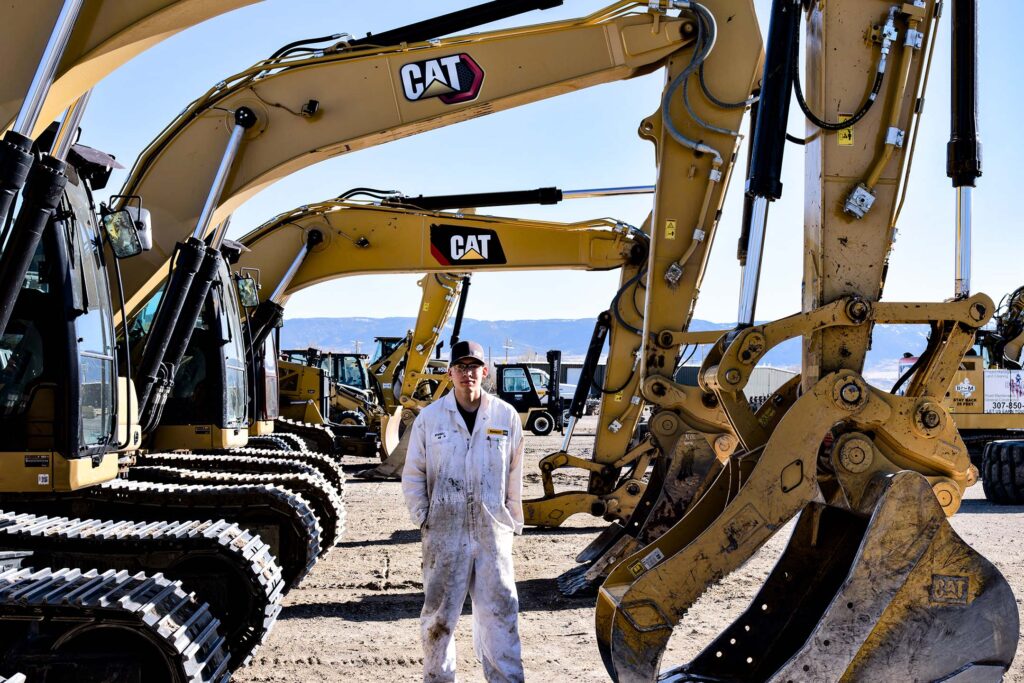 A student stands among CAT excavators during hands-on equipment training at Wyoming Machinery.