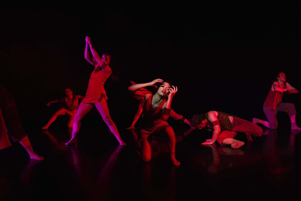 Contemporary dancers perform expressive choreography under dramatic red stage lighting.