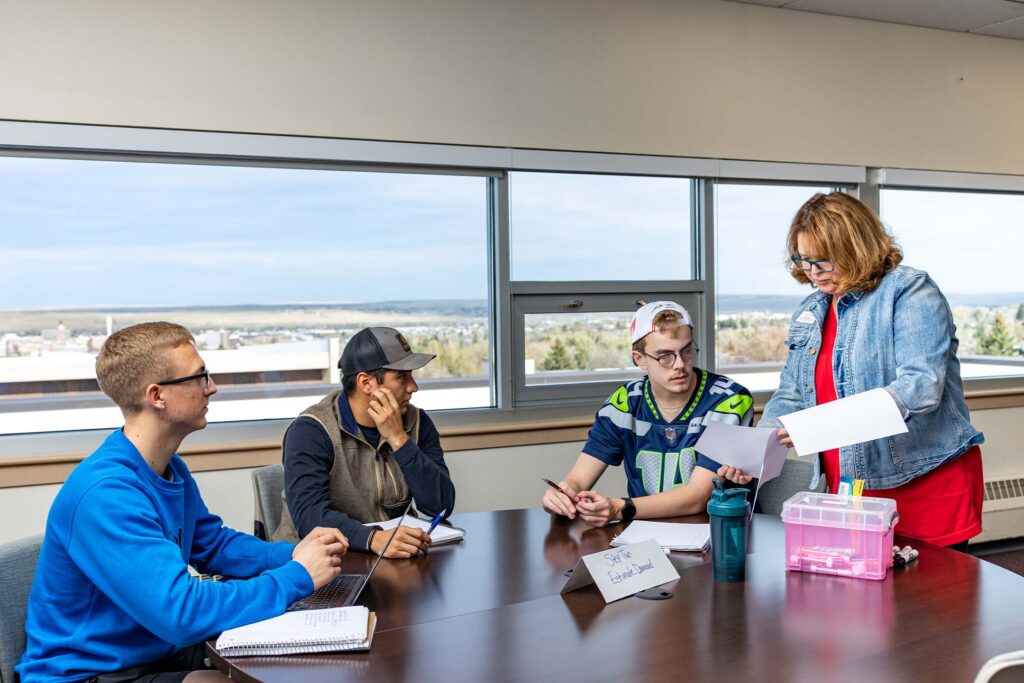Entrepreneurship students collaborate with their instructor to evaluate business ideas, develop solutions, and refine strategies through discussion and teamwork.