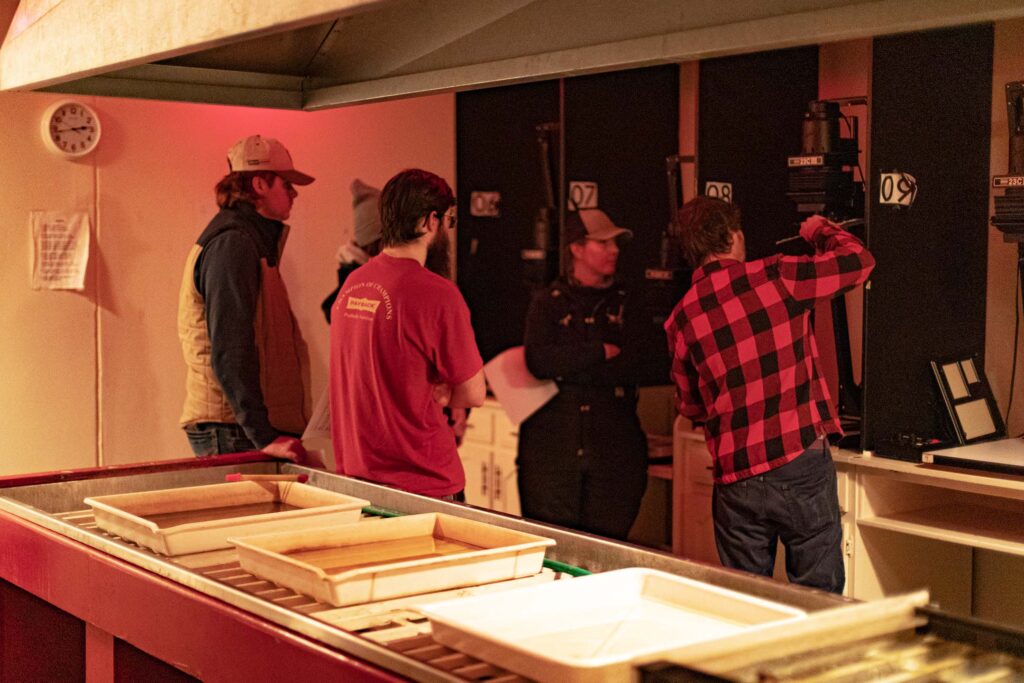 Photography students work together in a darkroom while learning traditional film processing techniques.