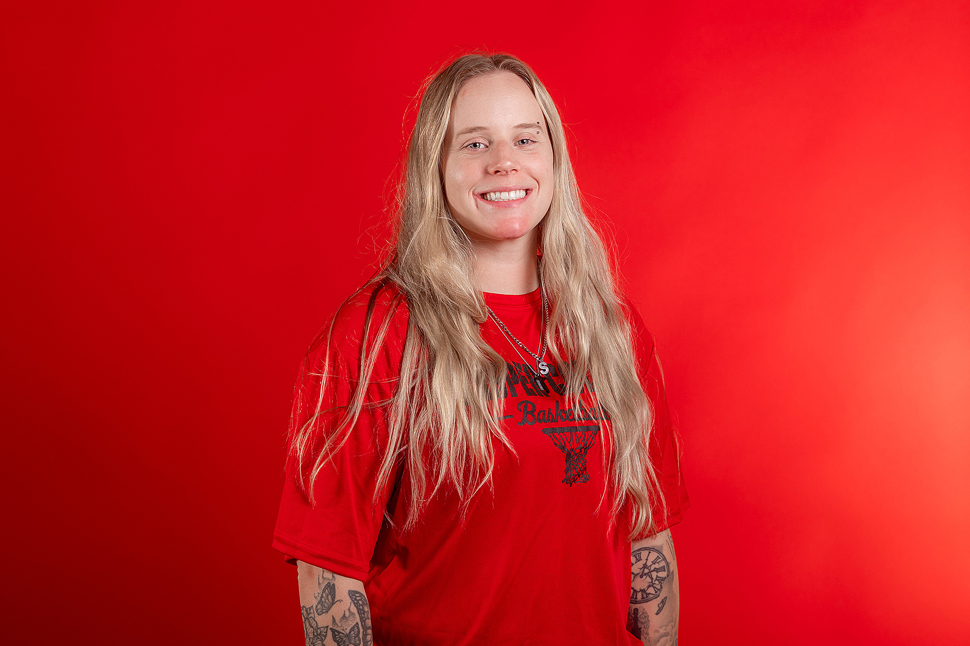 Maggie Justinak assistant coach smiling in a red basketball shirt against a red background.