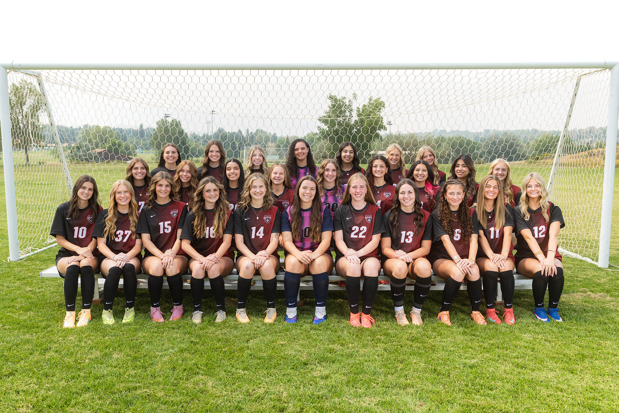 T-Bird women's soccer team in maroon and black uniforms posed in front of a goal on a soccer field.